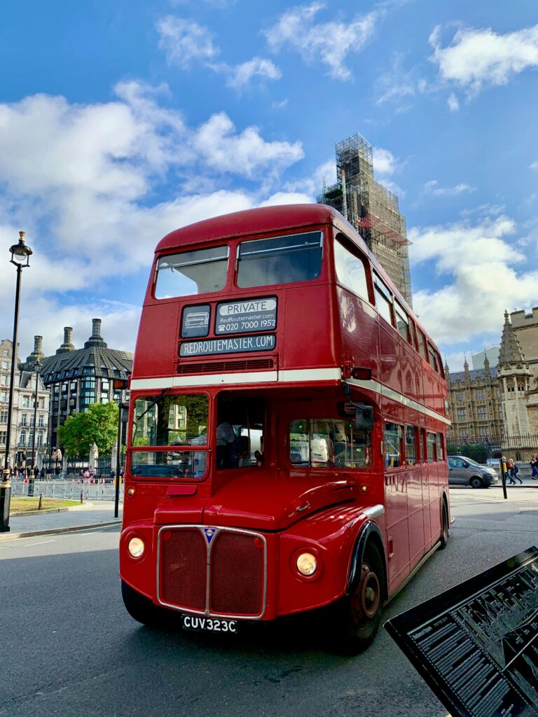 Classic London double-decker bus on a sunny day near famous landmarks.