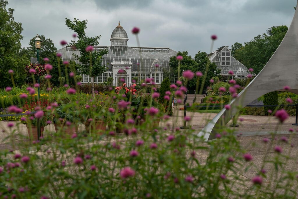 A beautifully designed glasshouse amidst vibrant gardens on a cloudy day, showcasing architectural elegance.
