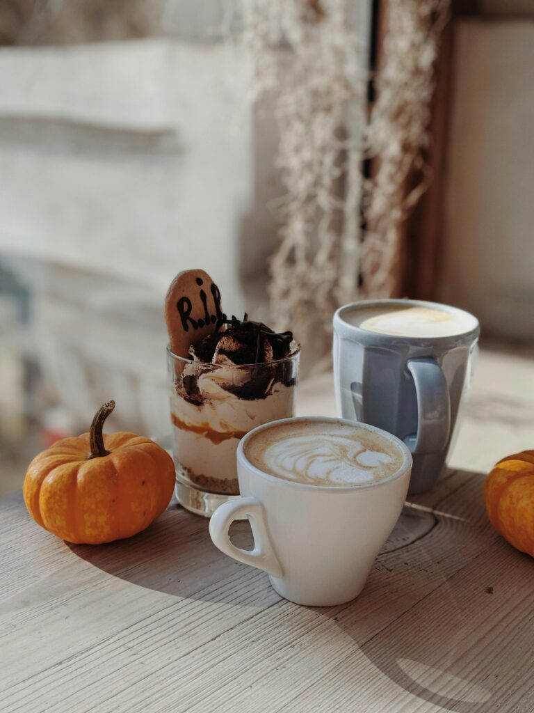 Warm autumn setup with coffee, dessert, and pumpkins on a wooden table.